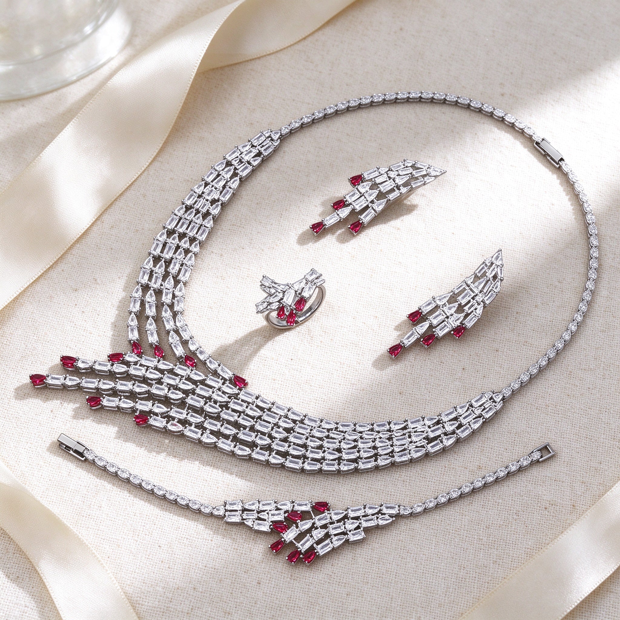 Styled flat lay of The Maeve Bridal Parure necklace, earrings, bracelet and ring on cream linen with an ivory ribbon
