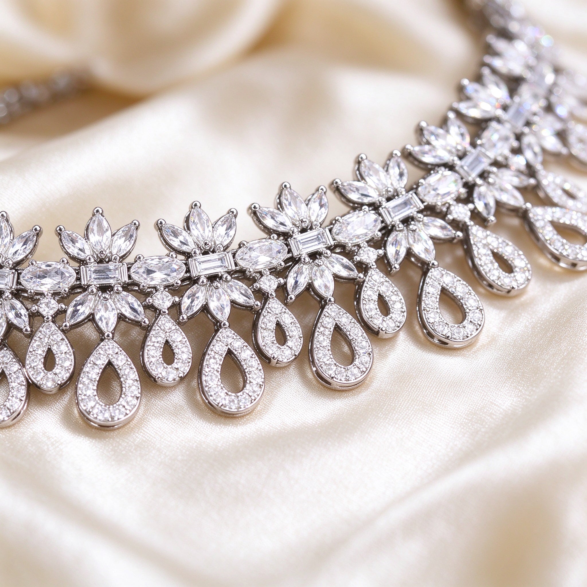 Macro of ornate floral CZ clusters with open teardrop pavé frames on silk