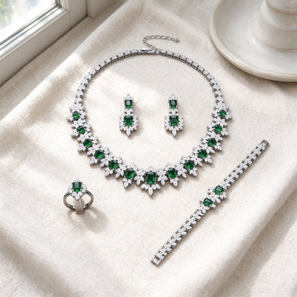 Top-down flat lay of The Twilight Bridal Parure four-piece silver emerald-green and clear CZ set on warm ivory linen