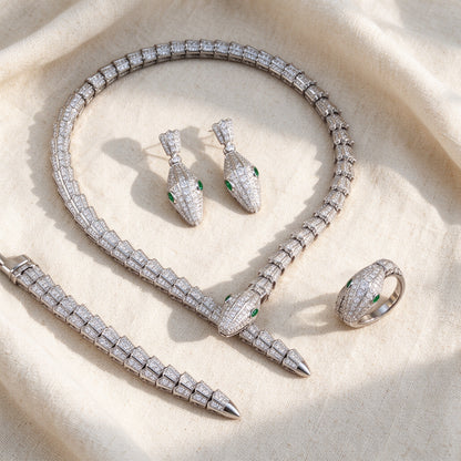 Top-down flat lay of The Lumina Crystal Set four-piece pavé serpent necklace, earrings, bracelet and ring on warm ivory linen