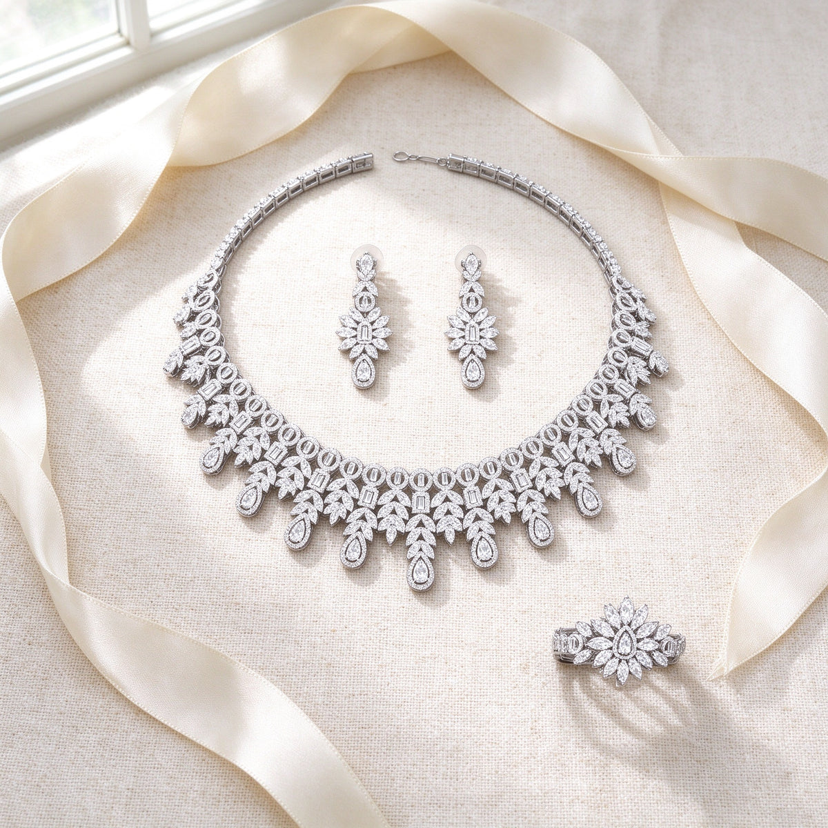 Styled flat lay of The Lyra Crystal Parure necklace, earrings, bracelet and ring on cream linen with an ivory ribbon