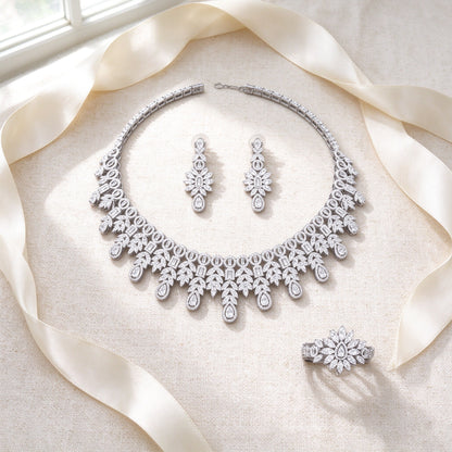 Styled flat lay of The Lyra Crystal Parure necklace, earrings, bracelet and ring on cream linen with an ivory ribbon