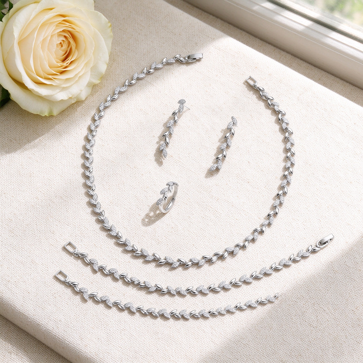 Flat lay of The Summit Wedding Suite necklace, earrings, bracelet and ring with ivory rose