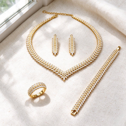 Top-down flat lay of The Daybreak Wedding Suite four-piece marquise-CZ laurel bridal set on warm ivory linen