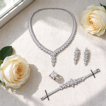 Flat lay of The Apex Crystal Parure necklace, earrings, bracelet and ring with ivory roses