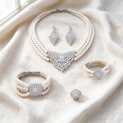 Flat lay of The Clover Crystal Parure — pearl necklace, earrings, bracelet, and ring arranged on ivory linen