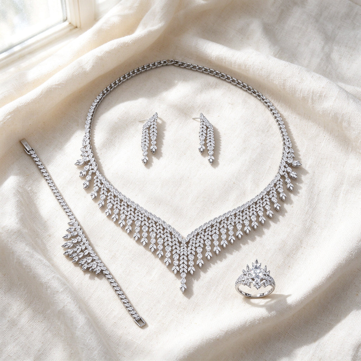 Flat lay of The Moss Bridal Set — fringe necklace, earrings, tennis bracelet, and solitaire ring on ivory linen