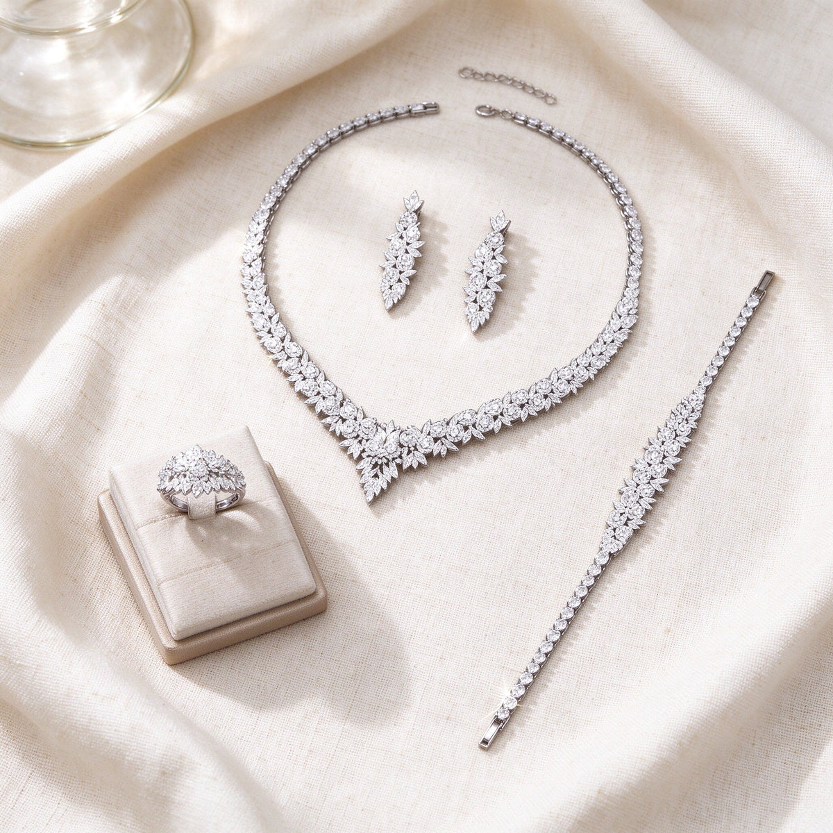 Flat lay of The Blair Crystal Parure necklace, earrings, tennis bracelet and ring on ivory linen