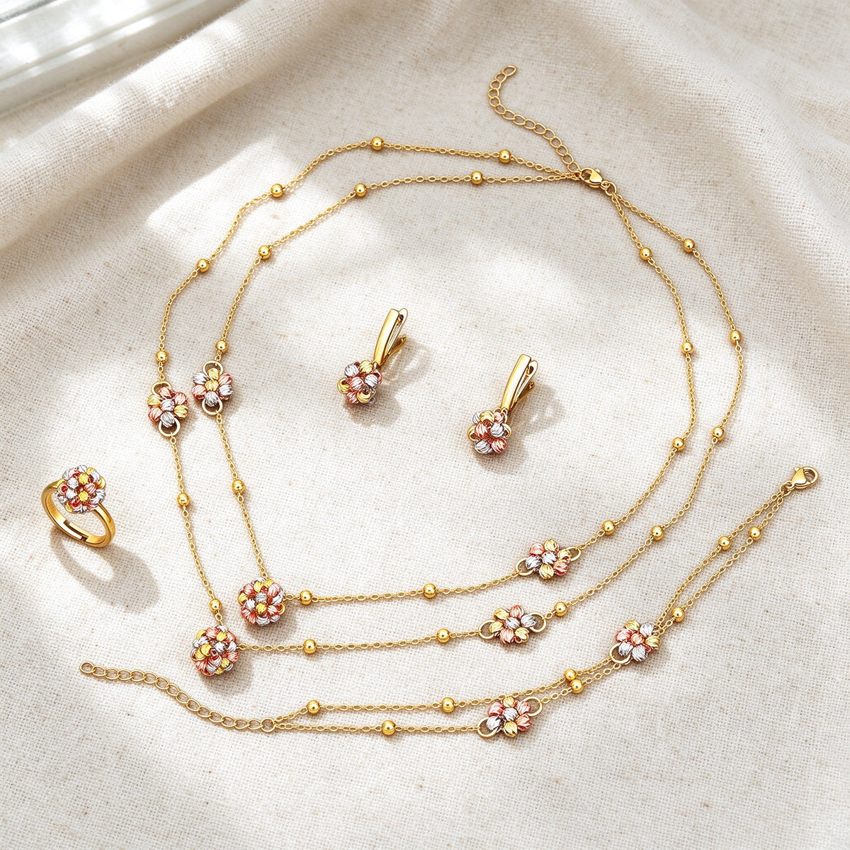 Top-down flat lay of The Sunbeam Crystal Parure four-piece dainty gold floral set on warm ivory linen