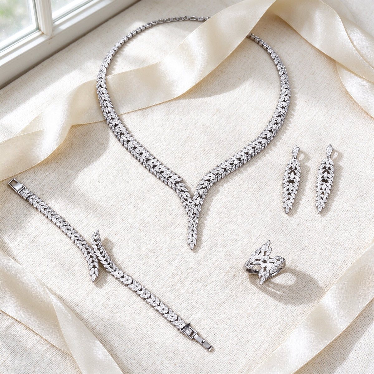 Styled flat lay of The Elowen Wedding Suite necklace, earrings, bracelet and ring on cream linen with an ivory ribbon