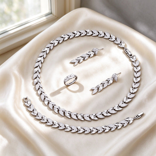 The Stella Bridal Parure silver-tone laurel-leaf botanical collar necklace, leaf drop earrings, ring and leaf-chain bracelet on ivory silk by a window