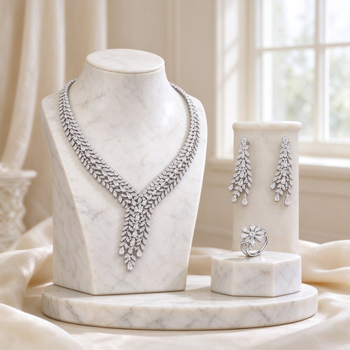 The Peyton Bridal Set - silver-tone cascading leaf-spray CZ V-necklace on an ivory marble bust, with drop earrings and floral cluster ring on cream pedestals