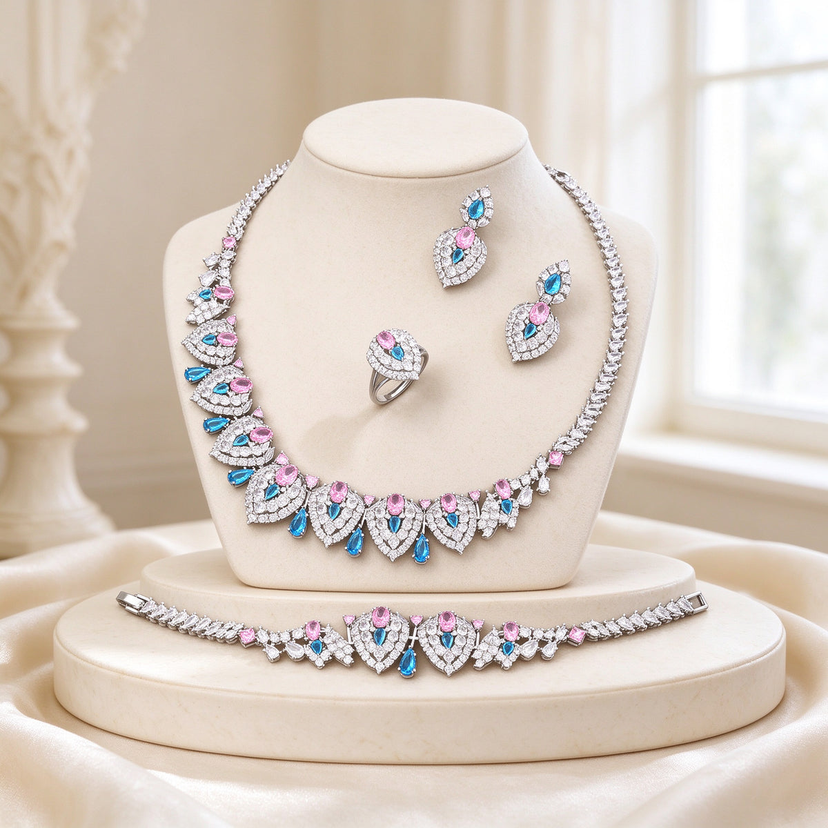 The Wren Wedding Suite - silver-tone teardrop-panel CZ statement necklace with rose-pink and azure-blue accents on an ivory bust, with earrings, bracelet and ring