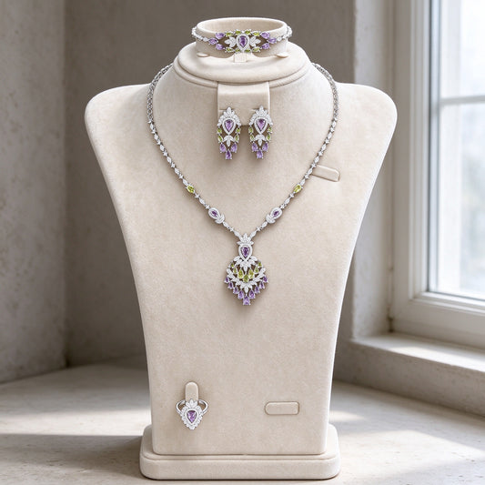 The Wheat Crystal Parure — silver-tone Y-necklace with amethyst-purple and peridot-green CZ chandelier pendant, earrings, bracelet and ring on cream velvet bust