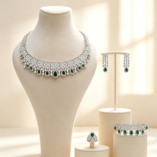 The Estelle Crystal Suite — silver-tone pavé collar necklace with emerald green pear teardrop fringe, chandelier earrings, bangle and cluster ring on ivory pedestals