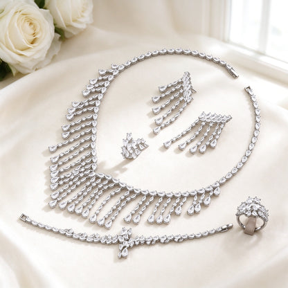 The Oriana Crystal Parure — silver-tone cascading pear and marquise CZ fringe bib necklace, long fringe-drop earrings, bracelet and cluster ring on an ivory background