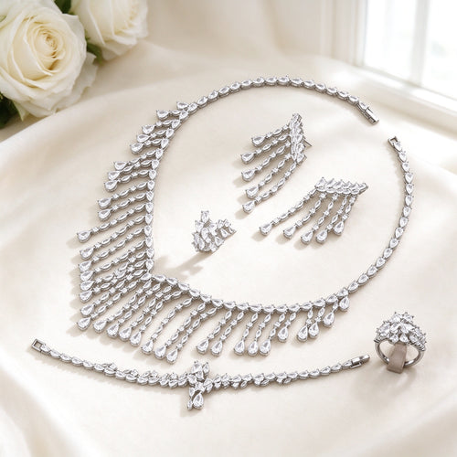 The Oriana Crystal Parure — silver-tone cascading pear and marquise CZ fringe bib necklace, long fringe-drop earrings, bracelet and cluster ring on an ivory background