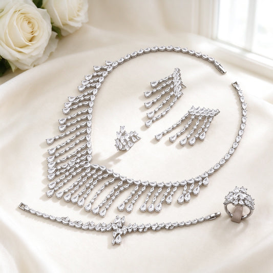 The Oriana Crystal Parure — silver-tone cascading pear and marquise CZ fringe bib necklace, long fringe-drop earrings, bracelet and cluster ring on an ivory background