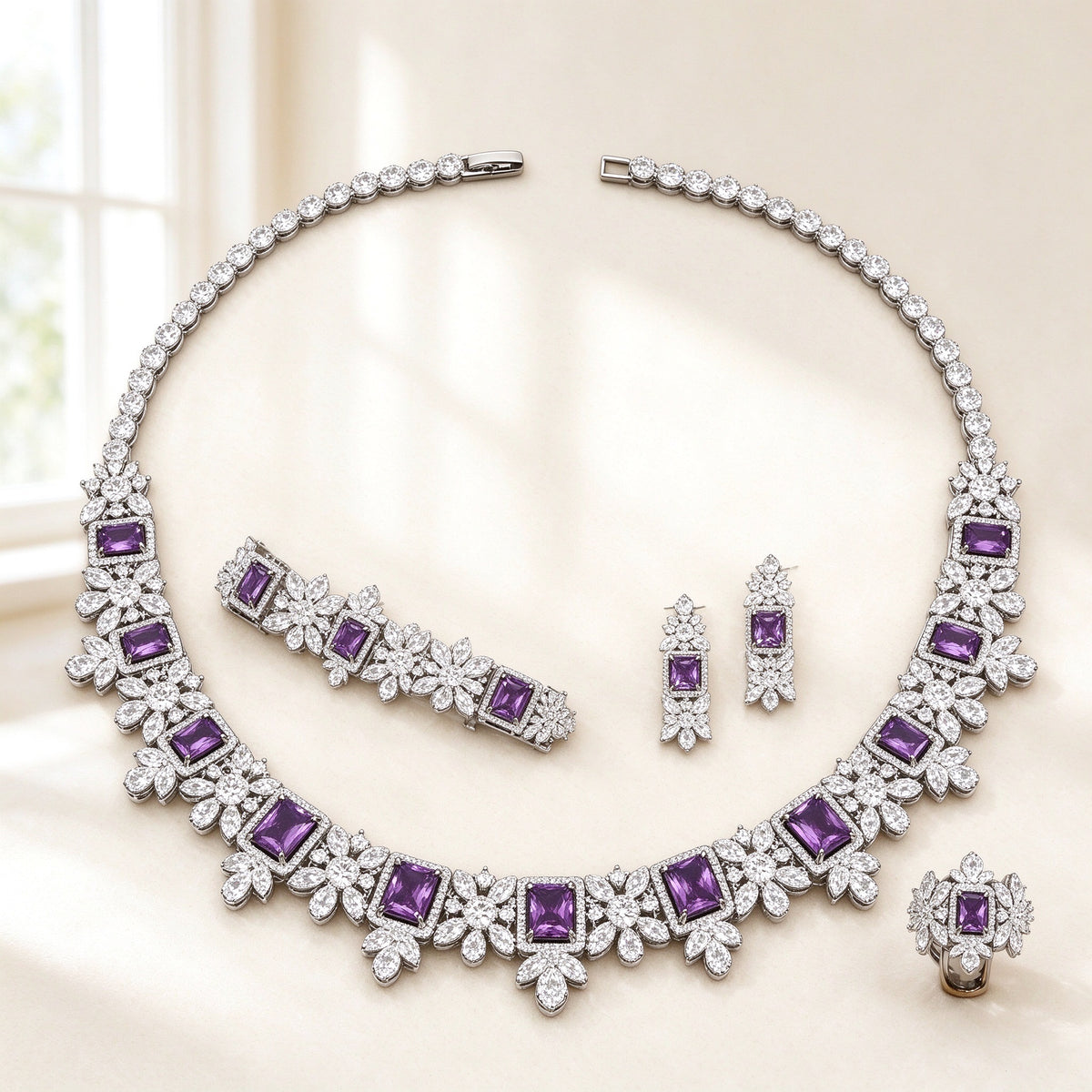 The Arabella Bridal Parure — silver-tone floral collar necklace with emerald-cut purple CZ stations, drop earrings, bracelet and ring on an ivory background