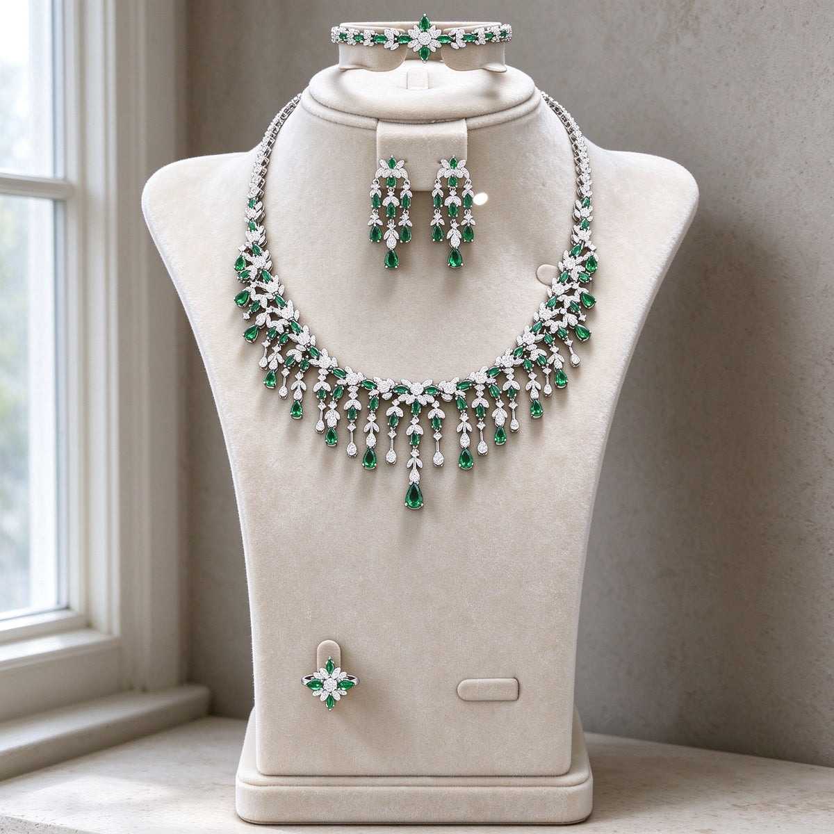 The Sheaf Wedding Suite — silver-tone fringe bib necklace with emerald-green CZ drops, three-tier chandelier earrings, bracelet and ring on cream velvet bust
