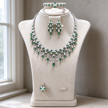 The Sheaf Wedding Suite — silver-tone fringe bib necklace with emerald-green CZ drops, three-tier chandelier earrings, bracelet and ring on cream velvet bust