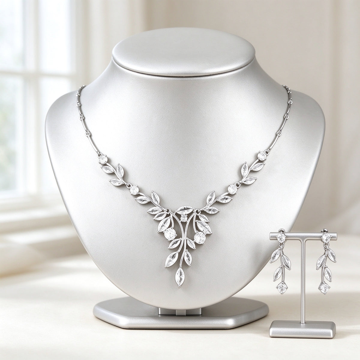 The Delaney Wedding Suite — silver-tone V-shaped botanical branch necklace with marquise leaf CZ and matching linear drop earrings on an ivory background