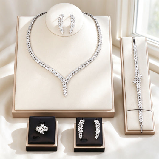 The Elara Crystal Parure – silver-tone V-shaped CZ tennis necklace, vine earrings, floral tennis bracelet and cluster ring on an ivory background