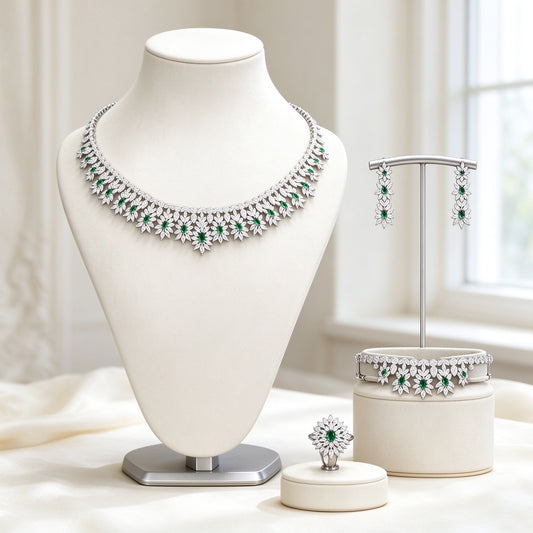 The Kennedy Crystal Parure — silver-tone floral sunburst collar necklace with emerald green CZ centers, earrings, tennis bracelet and sunburst ring on an ivory background