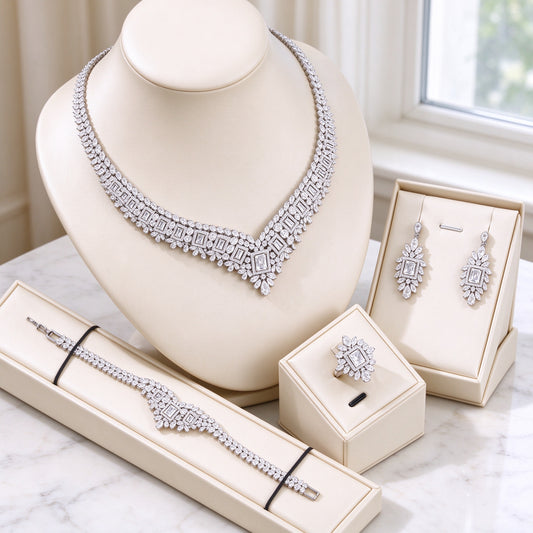 The Diadem Bridal Parure silver-tone pavé V-collar necklace, radiating drop earrings, floral halo ring and line bracelet on ivory leather bust over white marble