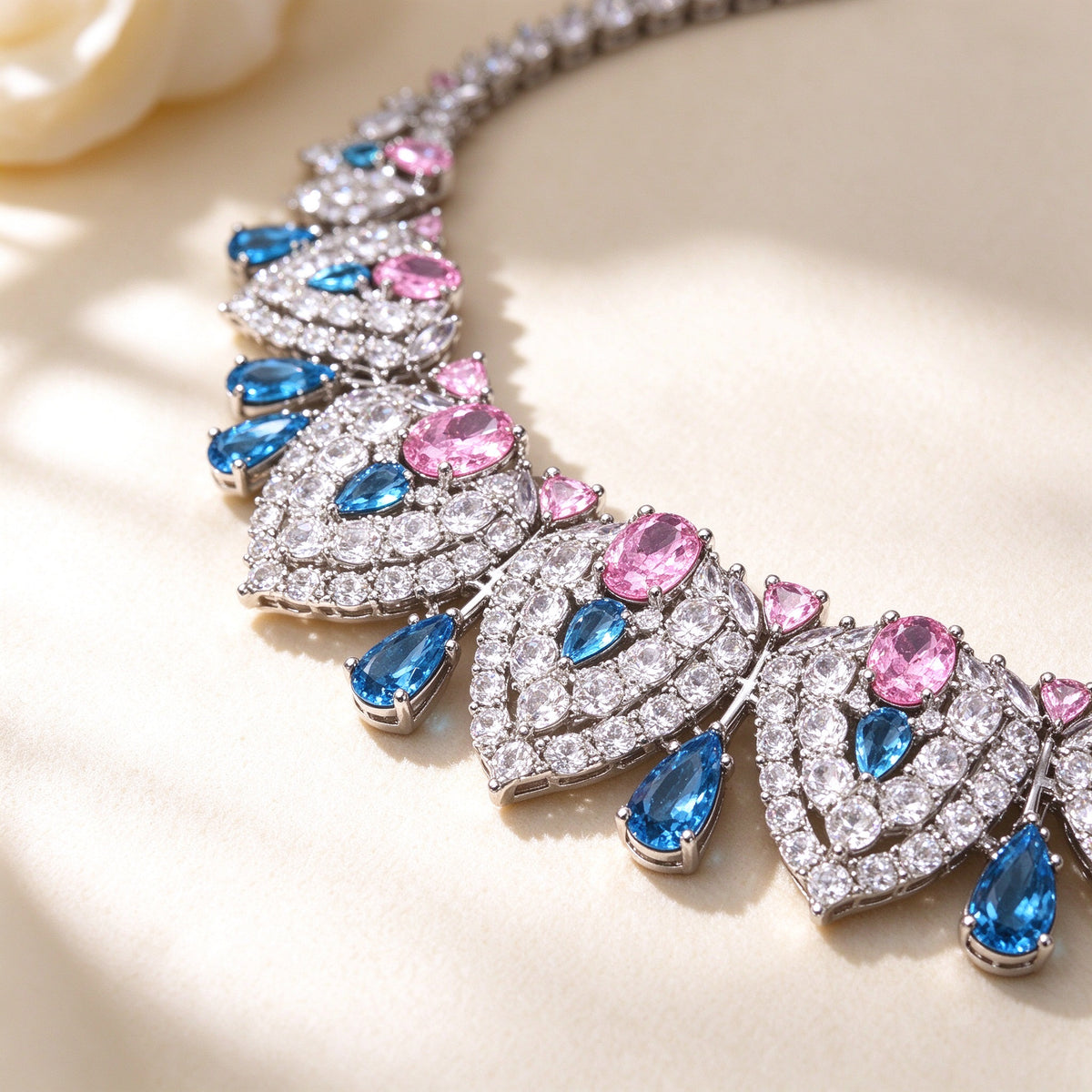 Macro close-up of The Wren clear-CZ teardrop panels centered with rose-pink and azure-blue stones on ivory silk