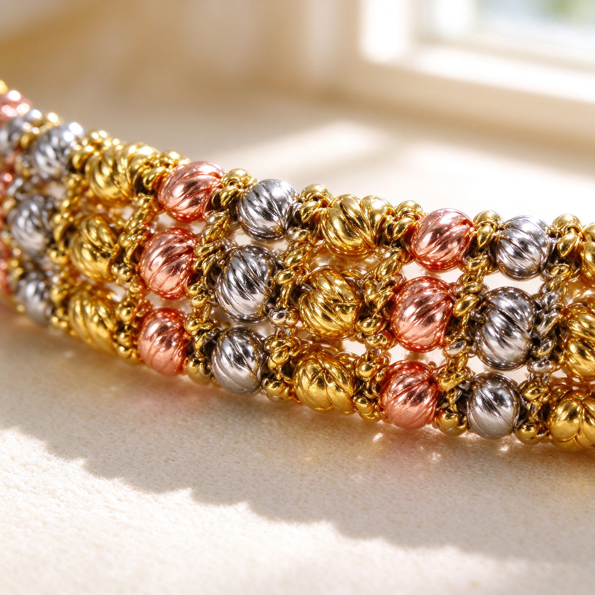 Macro close-up of The Emerson woven tri-tone metal beads in gold, rose gold and silver on ivory silk