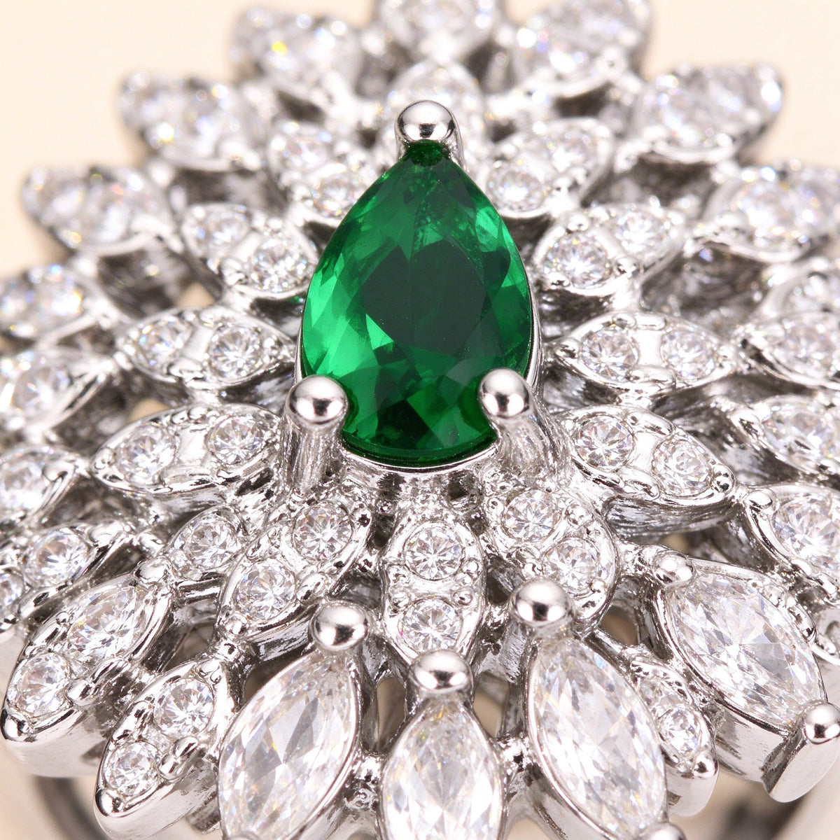 Macro close-up of an emerald green pear-shaped cubic zirconia surrounded by radiating clear marquise CZ petals