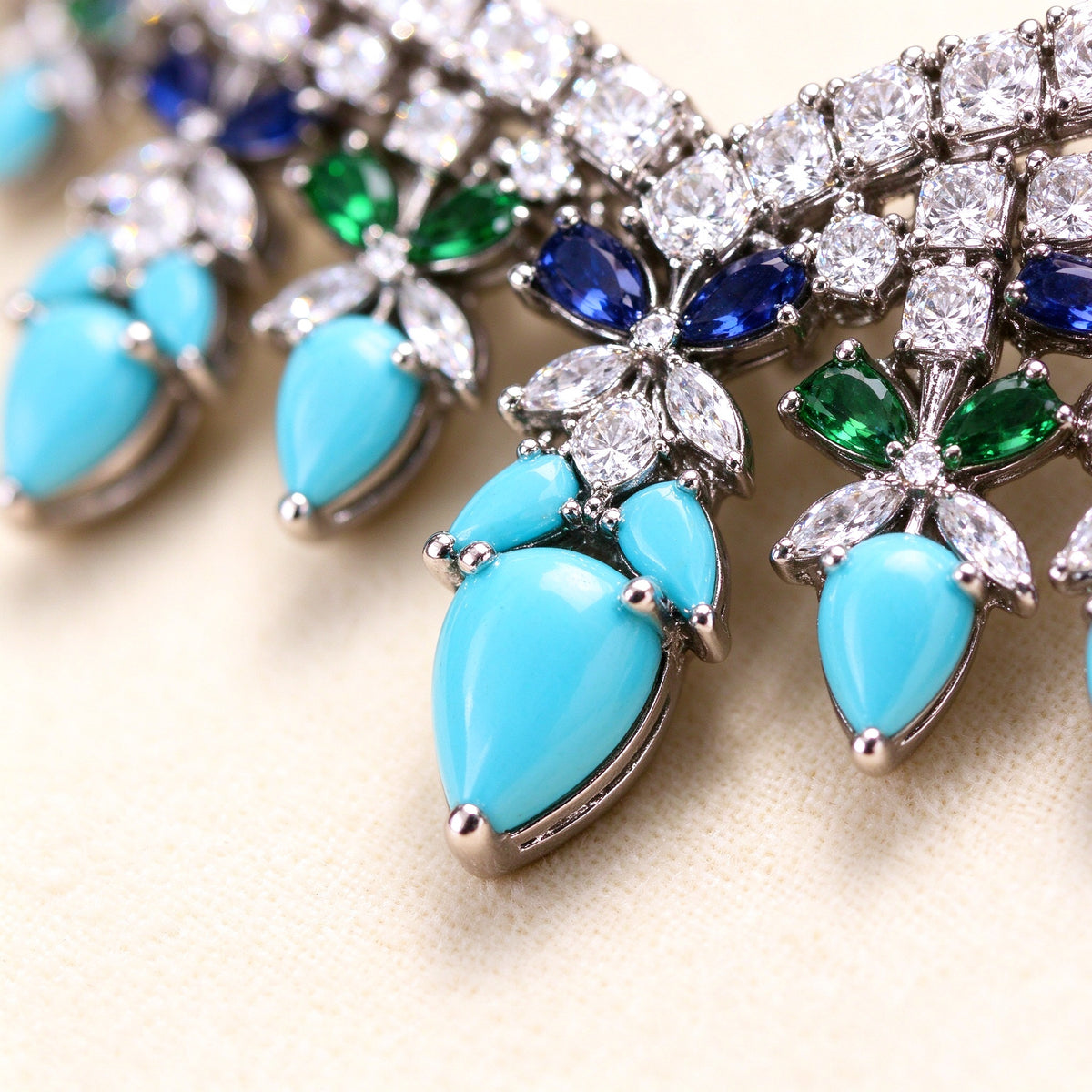 Macro close-up of a turquoise pear-shaped cubic zirconia drop surrounded by clear CZ pavé and blue/green marquise accents