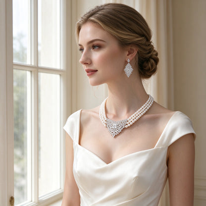 Caucasian bride wearing The Clover three-strand pearl necklace and leaf-cluster CZ earrings with an ivory silk gown by a sunlit window