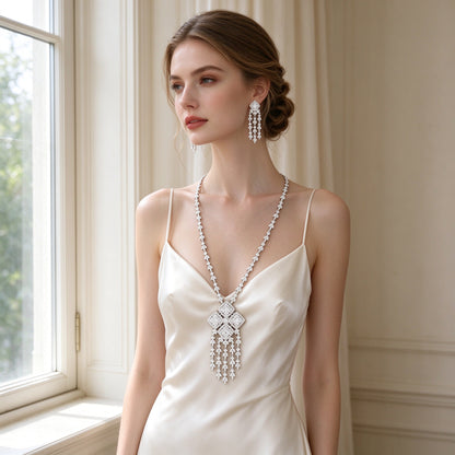 Caucasian bride wearing The Aster Bridal Set — long CZ tassel necklace and earrings with an ivory silk slip dress by a sunlit window