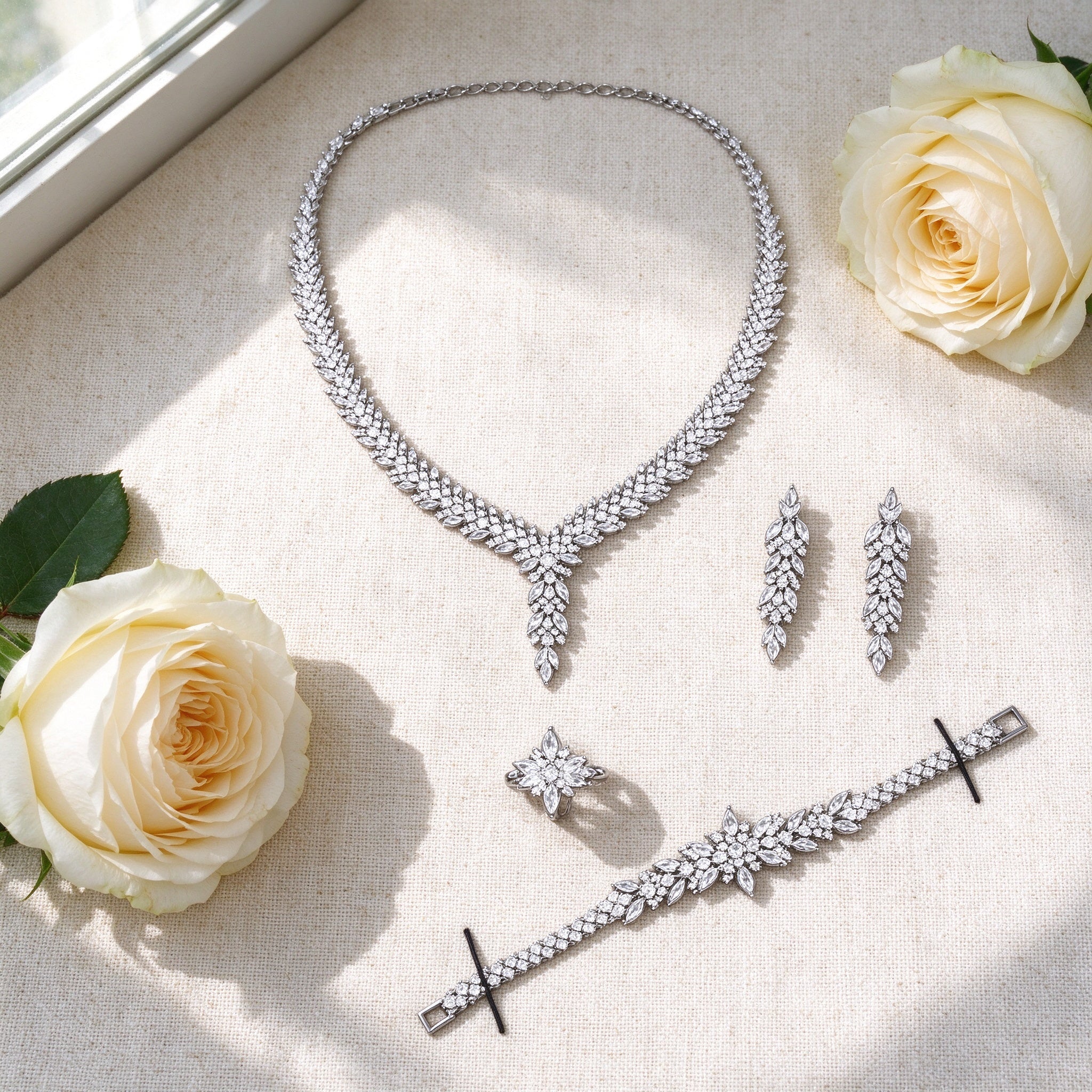 Flat lay of The Apex Crystal Parure necklace, earrings, bracelet and ring with ivory roses
