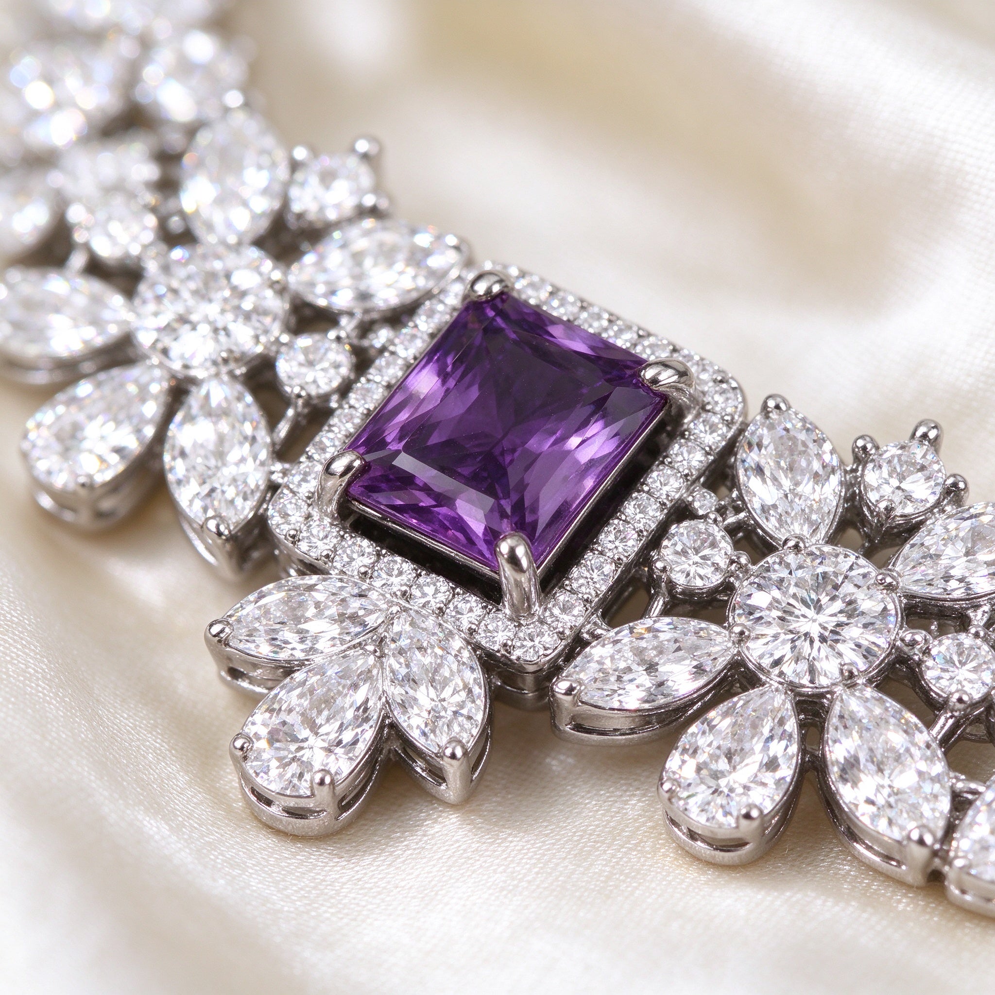 Macro close-up of an emerald-cut rectangular purple cubic zirconia framed by clear CZ floral clusters