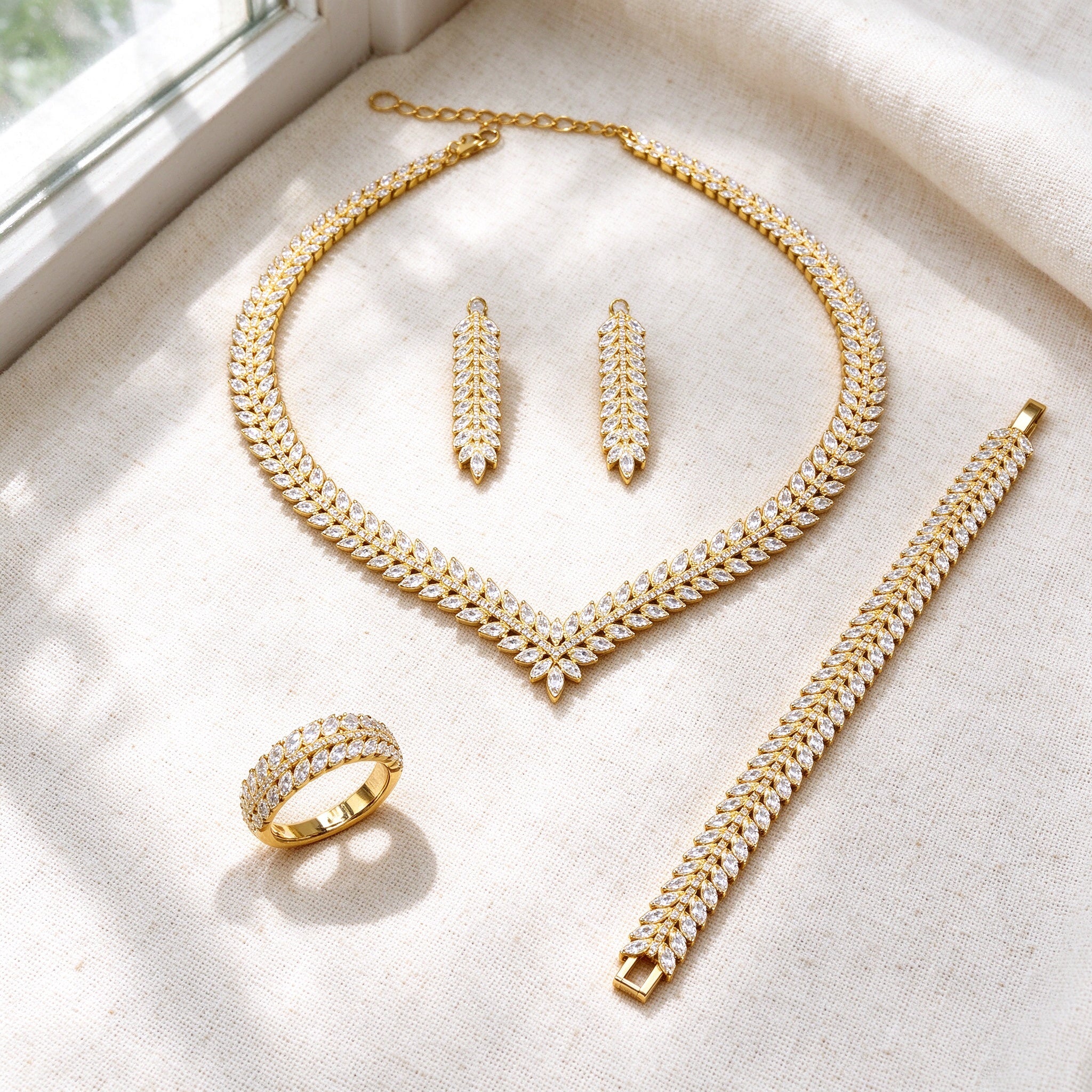 Top-down flat lay of The Daybreak Wedding Suite four-piece marquise-CZ laurel bridal set on warm ivory linen