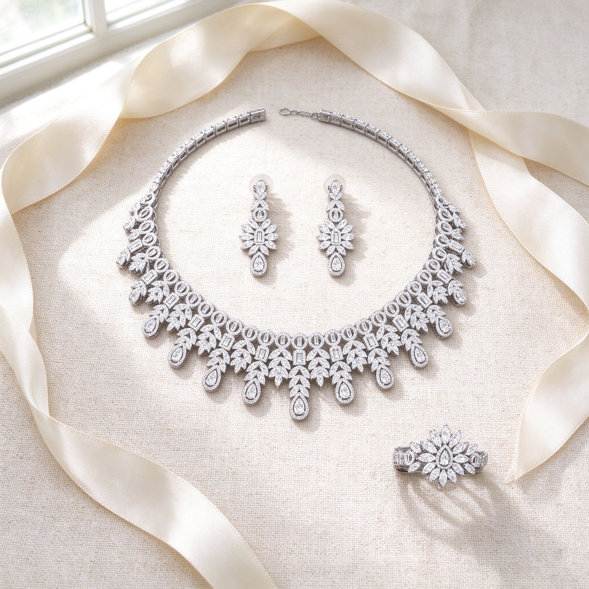 Styled flat lay of The Lyra Crystal Parure necklace, earrings, bracelet and ring on cream linen with an ivory ribbon