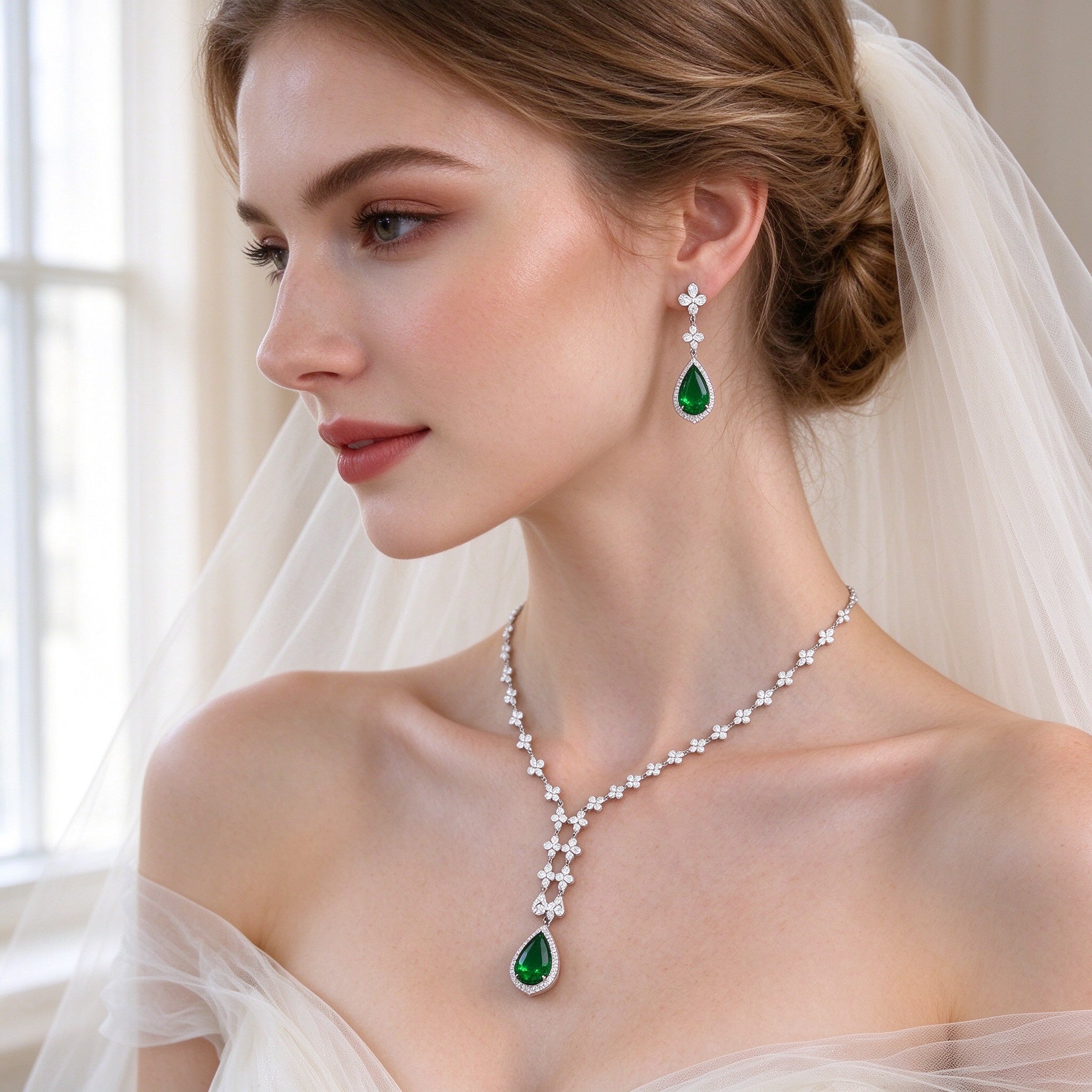 Three-quarter view of bride in ivory tulle veil wearing The Magnolia Crystal Parure green pendant necklace and drop earrings