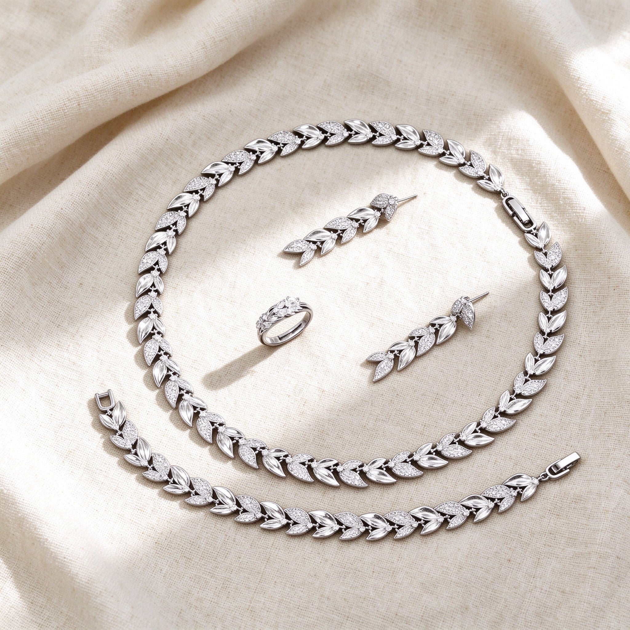 Top-down flat lay of The Stella Bridal Parure four-piece laurel-leaf botanical bridal set on warm ivory linen