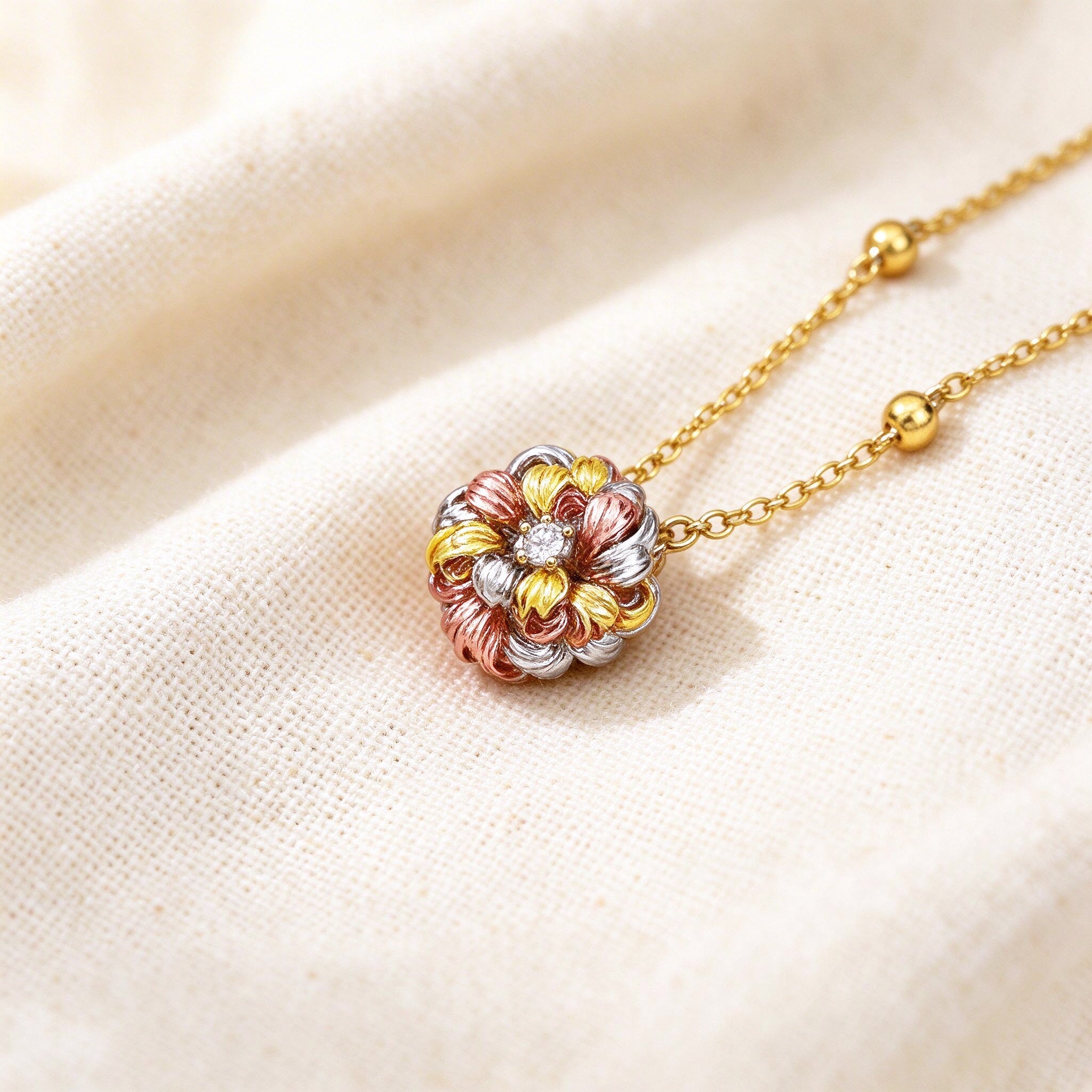 Macro detail of The Sunbeam Crystal Parure tiny three-dimensional tri-color flower charm on the gold ball-bead chain