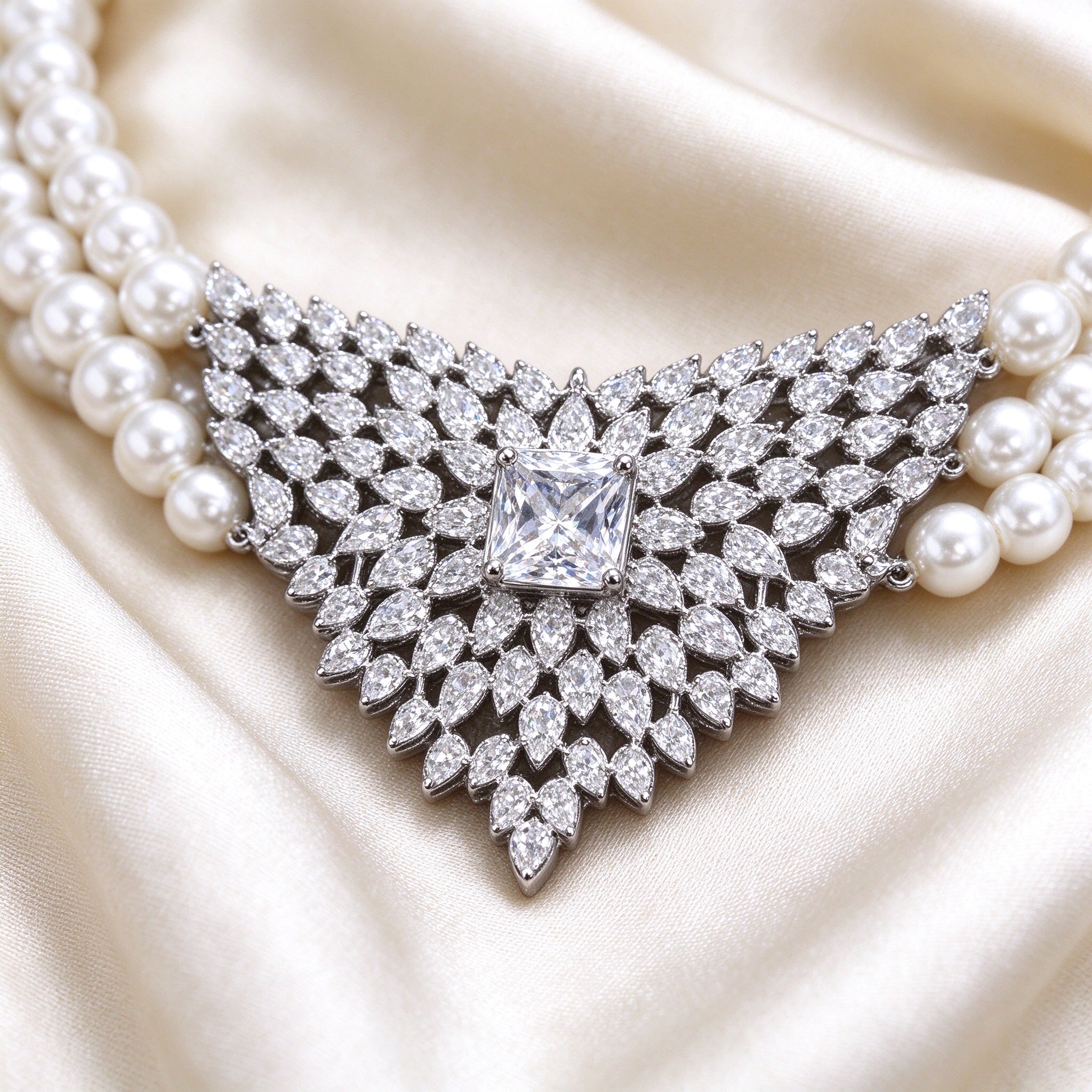 Macro detail of The Vale Bridal Parure V-shaped CZ pendant on pearl necklace