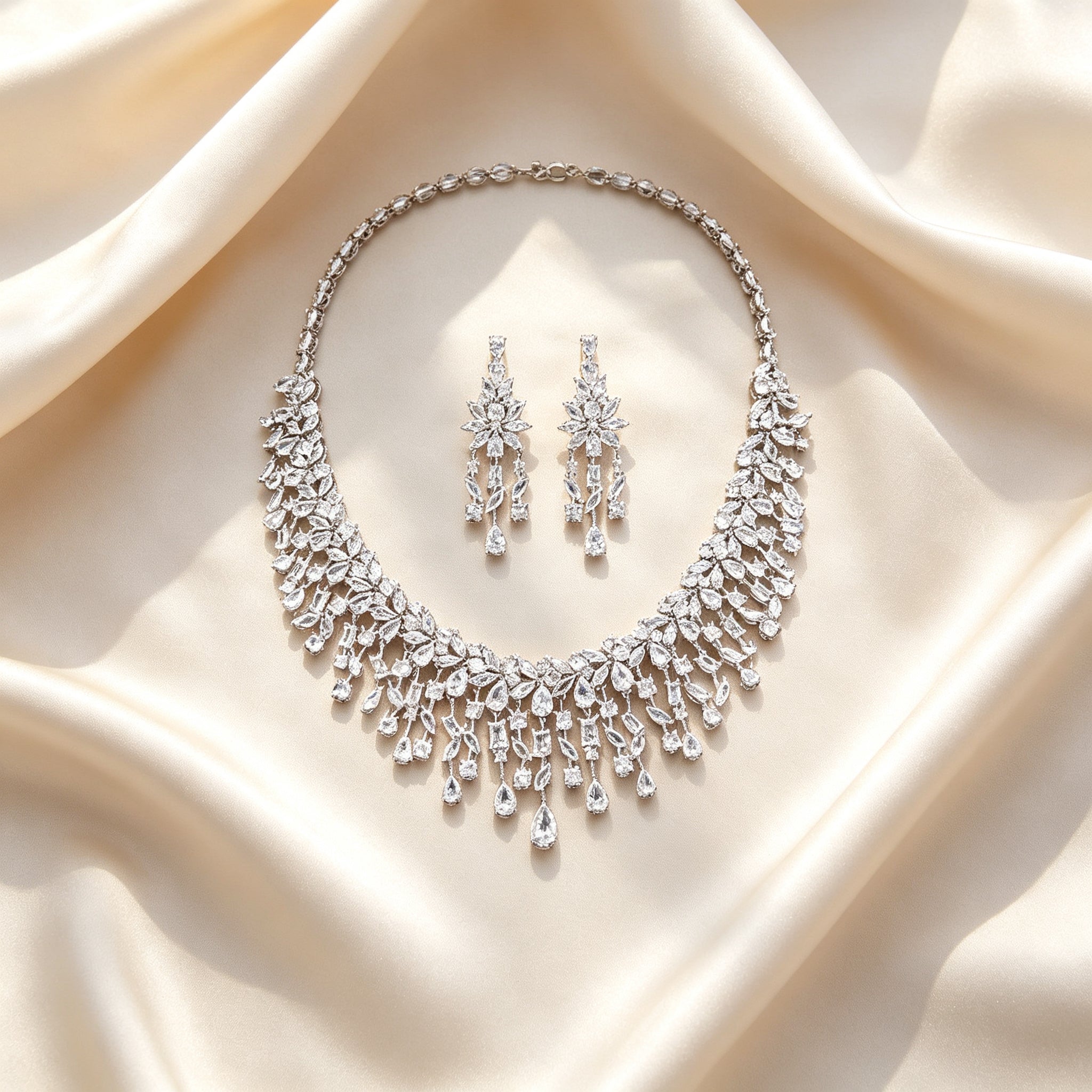 Flat lay of The Vivienne Bridal Parure necklace and earrings on draped ivory champagne silk